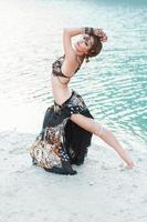 Beautiful girl dancing in tribal style on white sand beach near the water photo