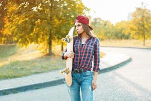 Pretty woman in shirt and jeans holding a skateboard. Beautiful portrait outdoors autumn evening at sunset photo