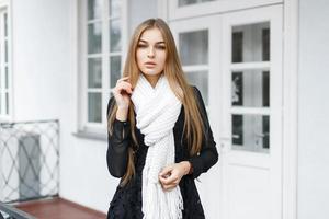 Stylish young beautiful girl in a black dress and a white knitted scarf on a light white background photo