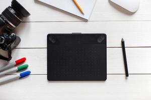 Concept of the artist Desktop. Graphics tablet, SLR camera, mouse, notebook, pencil and markers on a white wooden table. View from above photo