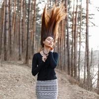 hermosa joven con un vestido negro de pie en el parque. pelo volando hacia arriba. foto