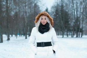 Beautiful girl  in a winter jacket stands in the park photo