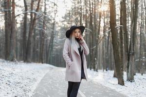Young beautiful girl in a stylish hat and coat walking in the winter park photo
