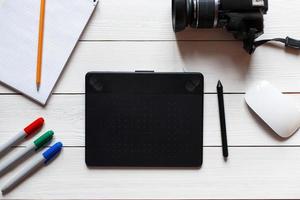 Concept artist desktop. Graphics tablet, camera, notebook with pencil and markers on a white wooden table. View from above photo