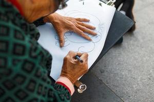 Elderly woman in glasses is drawing on paper. Hand holding a pencil photo