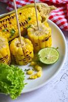 ripe corn cobs grilled sweetcorn for food vegan dinner or snack, sweet corn cooked on white plate, sweet corn food with salad vegetable lime coriander and lettuce photo