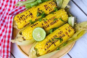 sweet corn cooked on wooden background, ripe corn cobs grilled sweetcorn for food vegan dinner or snack, sweet corn food with lime and coriander - top view photo