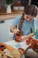 Little girl sitting at the table at home, sowing seeds into flower pots. photo