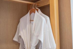 White clean bathrobe hanging in wooden wardrobe at luxury hotel or home. Relax and travel concept photo