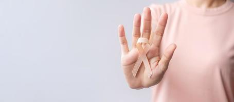 mano de mujer sosteniendo una cinta de melocotón para el mes de concientización sobre el cáncer uterino de septiembre. concepto de salud y día mundial del cáncer foto