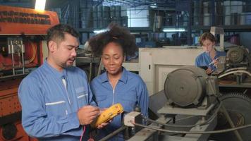 Asian male and female African American engineers in safety uniform work by inspecting machines' voltage current, checking, and maintaining at manufacture factory, electric system service occupations. video