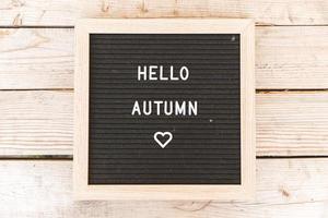 Autumnal Background. Black letter board with text phrase Hello Autumn lying on wooden palnks. Top view, flat lay. Thanksgiving banner. Hygge mood cold weather concept photo