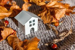 Autumnal Background. Toy house and dried orange fall maple leaves on grey knitted sweater. Thanksgiving banner copy space. Hygge mood cold weather concept. Hello Autumn with family photo