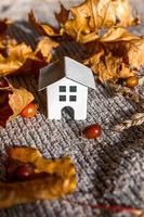 Autumnal Background. Toy house and dried orange fall maple leaves on grey knitted sweater. Thanksgiving banner copy space. Hygge mood cold weather concept. Hello Autumn with family photo