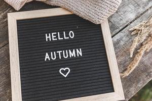 Autumnal Background. Black letter board with text phrase Hello Autumn and dried plant lying on wooden palnks. Top view, flat lay. Thanksgiving banner. Hygge mood cold weather concept photo