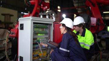 ingegnere industriale, lavoratore tecnico che indossa l'uniforme, elmetto di sicurezza che utilizza il computer tablet che controlla la macchina automatizzata del braccio robotico in fabbrica. concetto di industria manifatturiera automatica. video