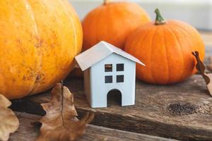 Autumnal Background. Toy house and pumpkin on wooden background. Thanksgiving banner copy space. Hygge mood, change of seasons concept. Hello Autumn with family Halloween party. photo