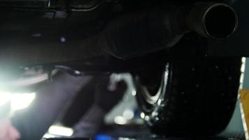 diagnóstico de automóviles - desatornillado mecánico trabajando bajo un camión levantado, fondo desenfocado, retroiluminación video
