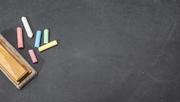 Group of colored chalk sticks and eraser on blackboard. Copy space. Back to school concept photo