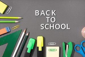 Back to school background. White phrase made of plastic letters and Variety of Office and school supplies on gray background photo