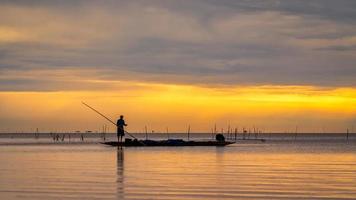 pescador asiático en bote de madera para pescar en el lago por la mañana foto