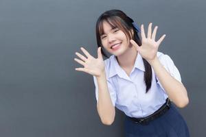 Beautiful Asian high school student girl in the school uniform with smiles confidently while she looks at the camera happily with grey in the background. photo