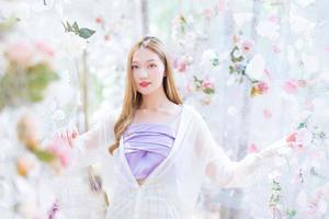 Asian beautiful woman blonde wearing a purple shirt while smiles and stands in white rose flower garden as natural , luxury theme photo