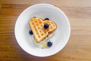 Tasty homemade Belgian waffles heart shaped on white bowl with berries and condensed milk. photo