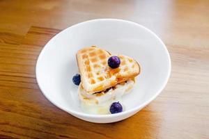 Tasty homemade Belgian waffles heart shaped on white bowl with berries and condensed milk. photo