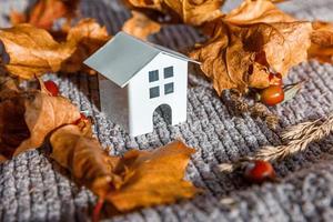 fondo otoñal. casa de juguetes y hojas secas de arce de otoño naranja en un suéter de punto gris. espacio de copia de banner de acción de gracias. concepto de clima frío de hygge mood. hola otoño en familia foto