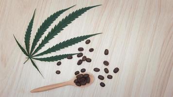 Coffee beans in a wooden spoon with cannabis leaves on a wooden table.copy space.flat lay.top-down.top view. photo