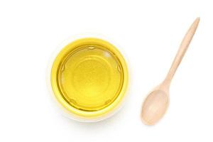 aceite vegetal amarillo en un recipiente transparente con una cuchara de madera sobre un fondo blanco. vista superior, de arriba hacia abajo, plano. foto