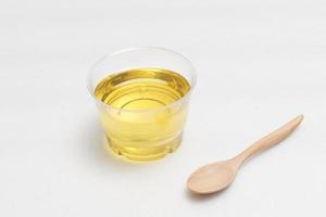 aceite vegetal amarillo en un recipiente transparente con una cuchara de madera sobre un fondo blanco. foto