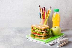 Healthy lunch for school with sandwich, fresh apple and orange juice. Assorted colorful school supplies. Copy space. photo