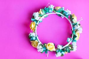 Circle of artificial crown from yellow and blue roses on pink background. photo