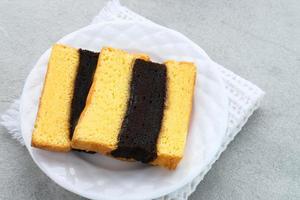 Spiku or Lapis Surabaya or Surabaya Layer Cake is a three-layer sponge cake with strawberry jam in between. Served in white plate, close up. photo