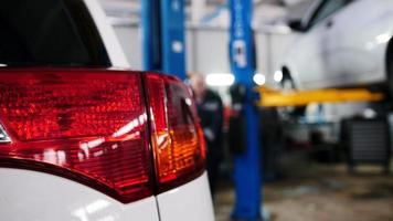 Car details - red auto headlight close up in diagnostic service - mechanic working near lifted car, slider video