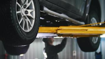 Car lifted in automobile service for fixing, worker repairs detail video
