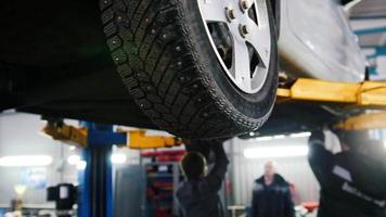 Car lifted in automobile service for repairing, workers fixing faults, video