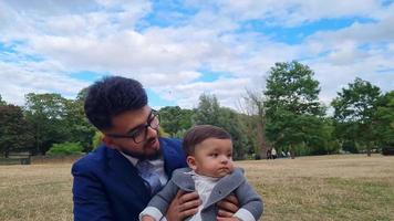 Aziatische Pakistaanse vader houdt zijn 11 maanden oude kind vast in een lokaal openbaar park dat Wardown Museum Park wordt genoemd, gelegen aan de New Bedford Road Luton Engeland, VK video