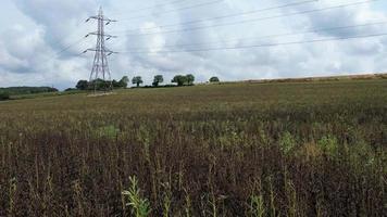 postes de suministro de energía de alto voltaje con cables que recorren las tierras de cultivo y el campo británicos, vista aérea de ángulo alto por la cámara de drones video