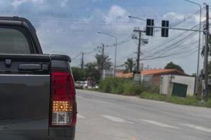 parte trasera del coche de recogida de color gris en la carretera asfaltada. prepárese para girar a la derecha en la señal derecha en la intersección con semáforos. imagen de fondo de un pequeño pueblo con césped y árboles. foto