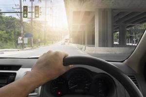 Hand of driving man with console of car inside interior view.  Looking ahead on a junction with a green traffic light. Above is a concrete bridge. photo