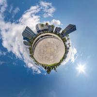 tiny planet in blue sky with clouds in city center near modern skyscrapers or office buildings. Transformation of spherical 360 panorama in abstract aerial view. photo