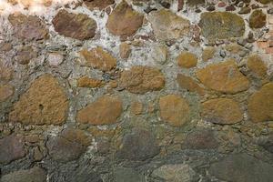 superficie de pared gris de piedras antiguas con yeso en grietas. foto