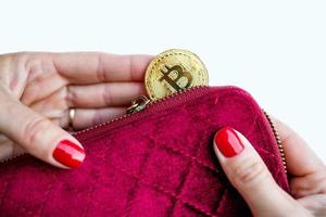 dinero virtual bitcoin dorado en monedero de tela de mujer rosa. dedos con uñas rojas en una moneda aislada de fondo blanco foto