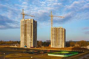 Tower cranes and unfinished multi-storey high near buildings under construction site in morning sun rays photo