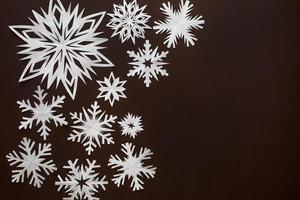 White paper snowflakes different shapes and sizes on brown cardboard background. Top view. photo