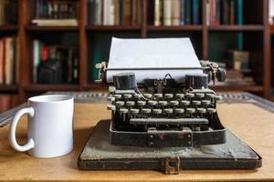 old vintage dust-covered typewriter with sheet of white paper and cup of coffee photo