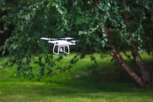 Quadrocopter volador blanco con cámara sobre fondo de bosque verde foto